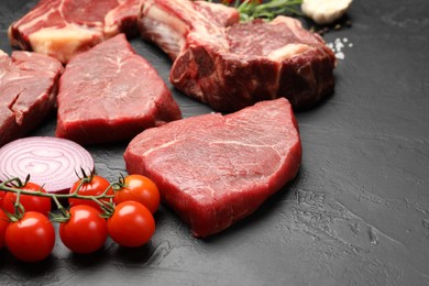 Photo of Pieces of raw beef meat, spices and tomatoes on black table, closeup. Space for text