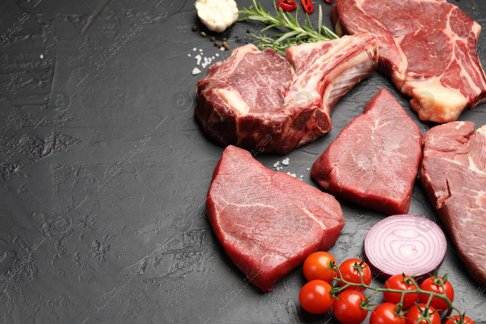Photo of Pieces of raw beef meat, spices and tomatoes on black table, above view. Space for text
