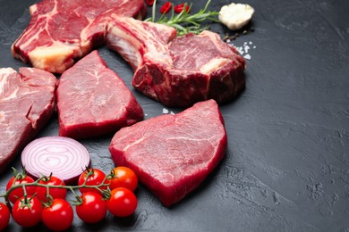 Photo of Pieces of raw beef meat, spices and tomatoes on black table, closeup. Space for text