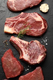 Photo of Pieces of raw beef meat and spices on black table, flat lay