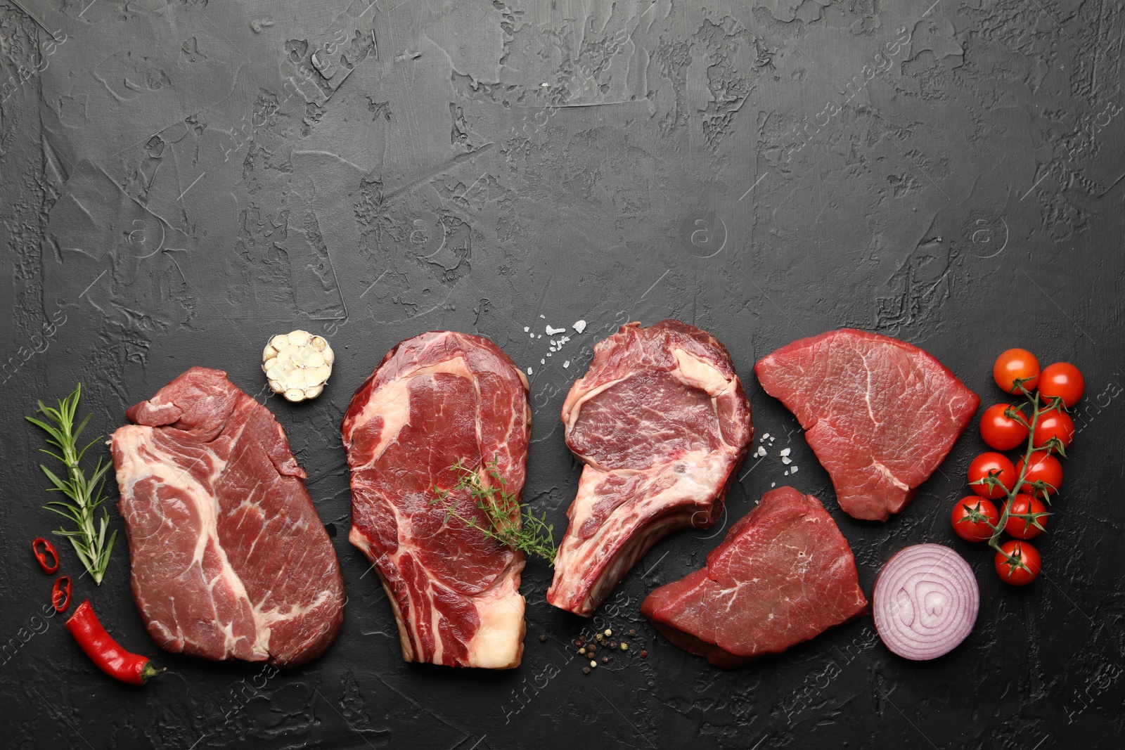Photo of Pieces of raw beef meat, spices and tomatoes on black table, flat lay. Space for text