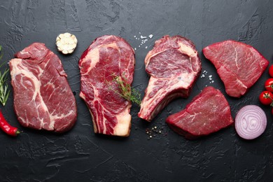 Photo of Pieces of raw beef meat, spices and tomatoes on black table, flat lay