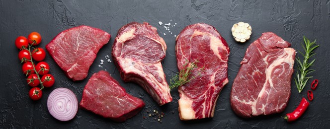 Photo of Pieces of raw beef meat, spices and tomatoes on black table, flat lay