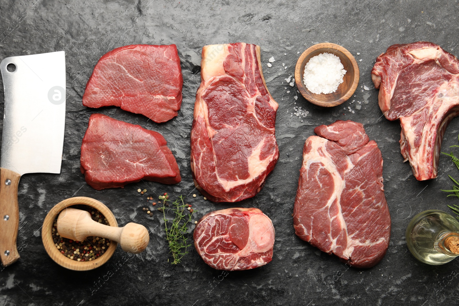 Photo of Pieces of raw beef meat, spices and cleaver on black marble table, flat lay