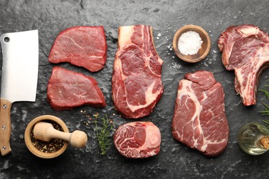 Photo of Pieces of raw beef meat, spices and cleaver on black marble table, flat lay