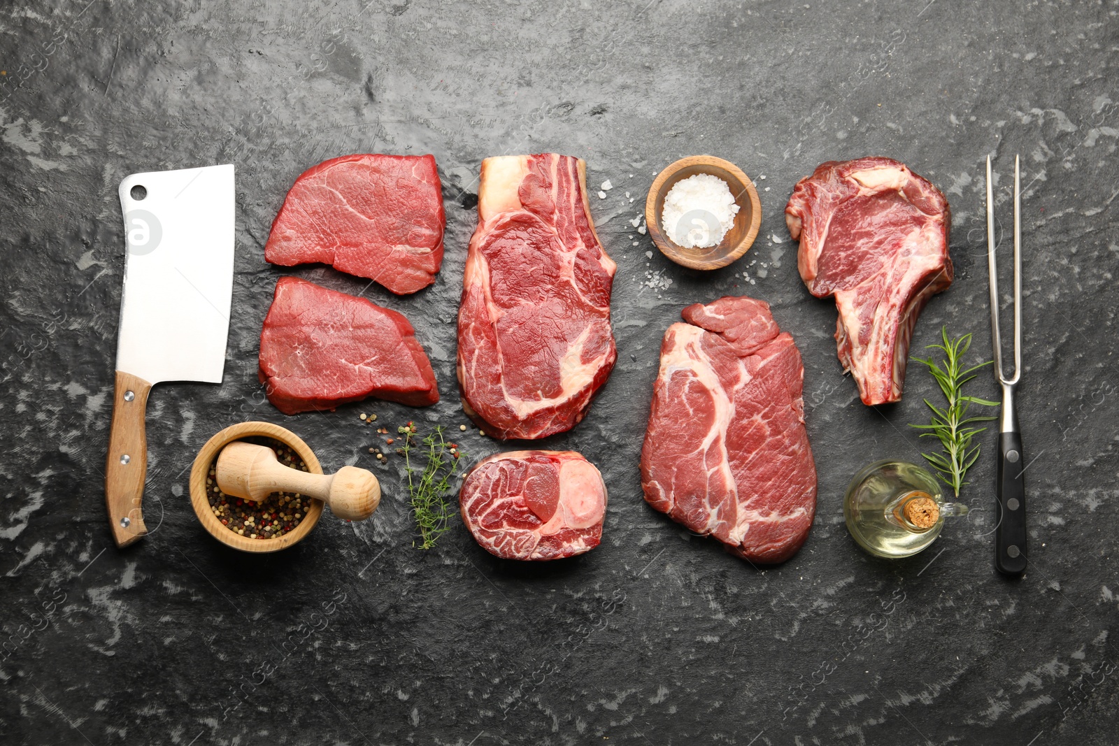Photo of Pieces of raw beef meat, spices, carving fork and cleaver on black marble table, flat lay