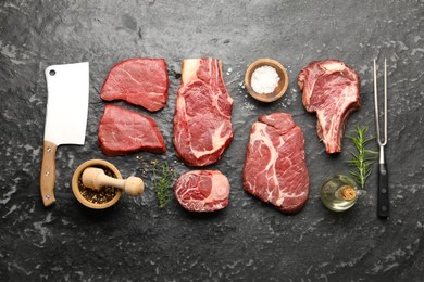 Photo of Pieces of raw beef meat, spices, carving fork and cleaver on black marble table, flat lay