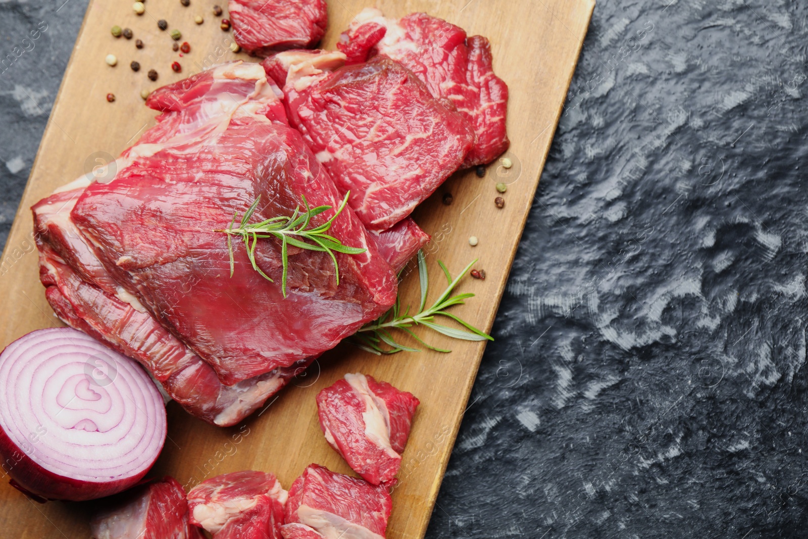 Photo of Pieces of raw beef meat and spices on black marble table, top view. Space for text