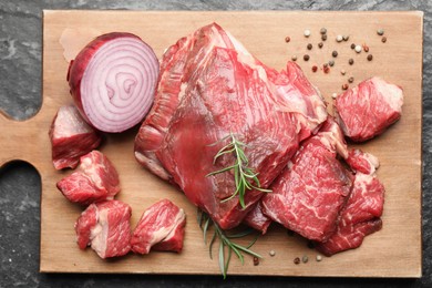 Photo of Pieces of raw beef meat and spices on black marble table, top view