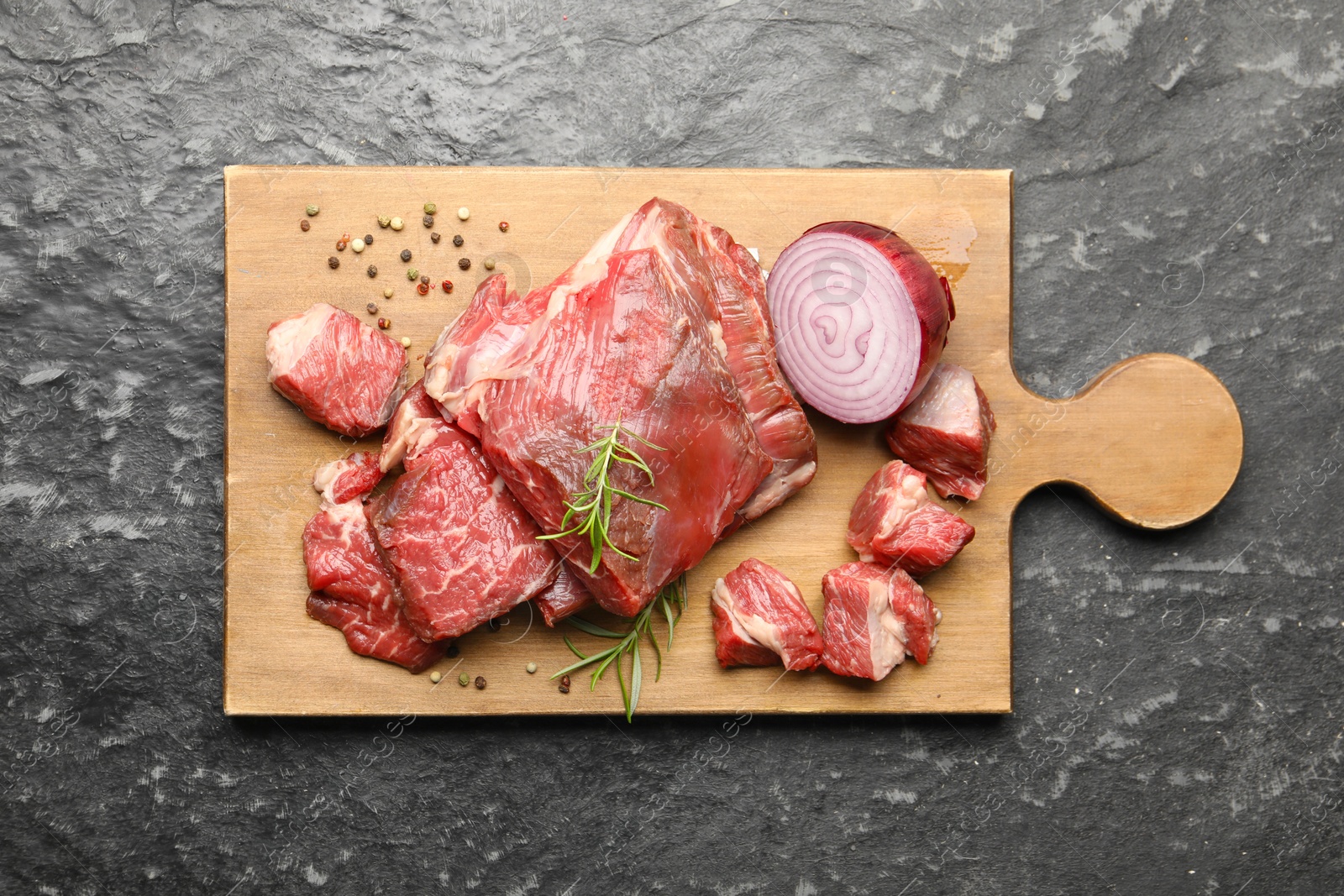 Photo of Pieces of raw beef meat and spices on black marble table, top view