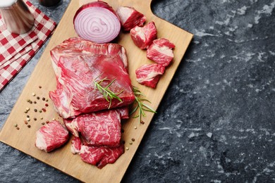 Photo of Pieces of raw beef meat and spices on black marble table, top view. Space for text