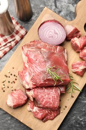 Photo of Pieces of raw beef meat and spices on black marble table, top view