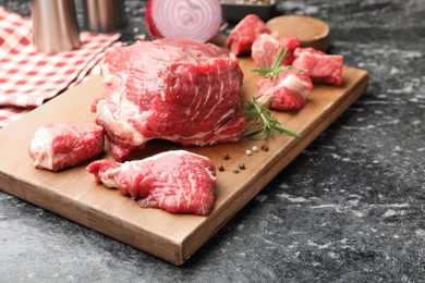 Photo of Pieces of raw beef meat and spices on black marble table, closeup