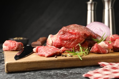 Photo of Pieces of raw beef meat, spices and knife on black marble table, closeup