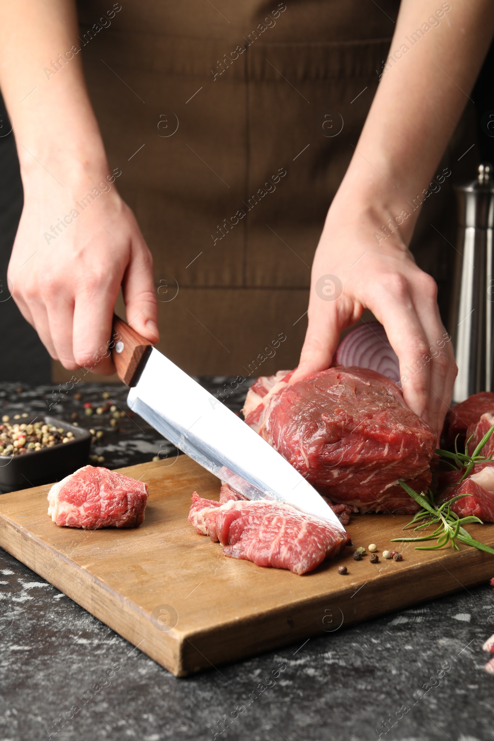 Photo of Woman cutting raw beef meat at dark table, closeup
