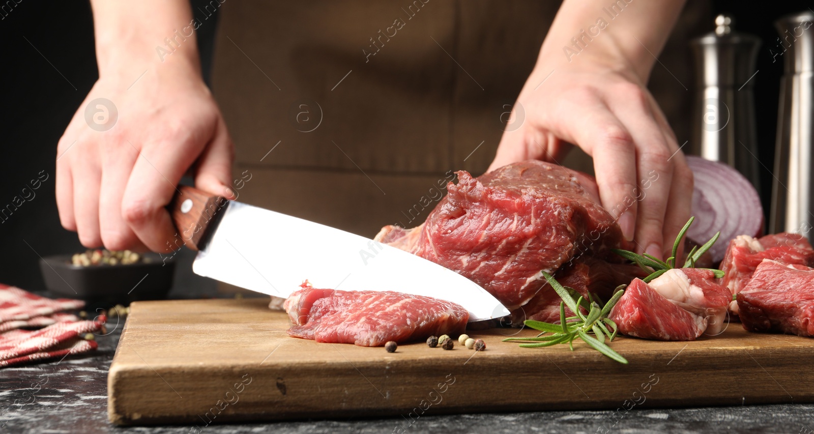 Photo of Woman cutting raw beef meat at dark table, closeup