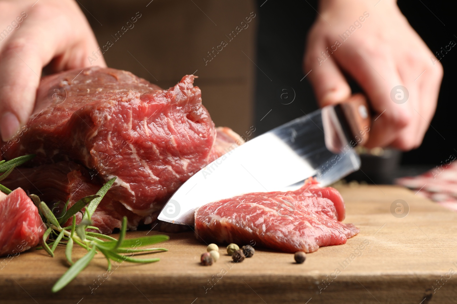 Photo of Woman cutting raw beef meat at table, closeup
