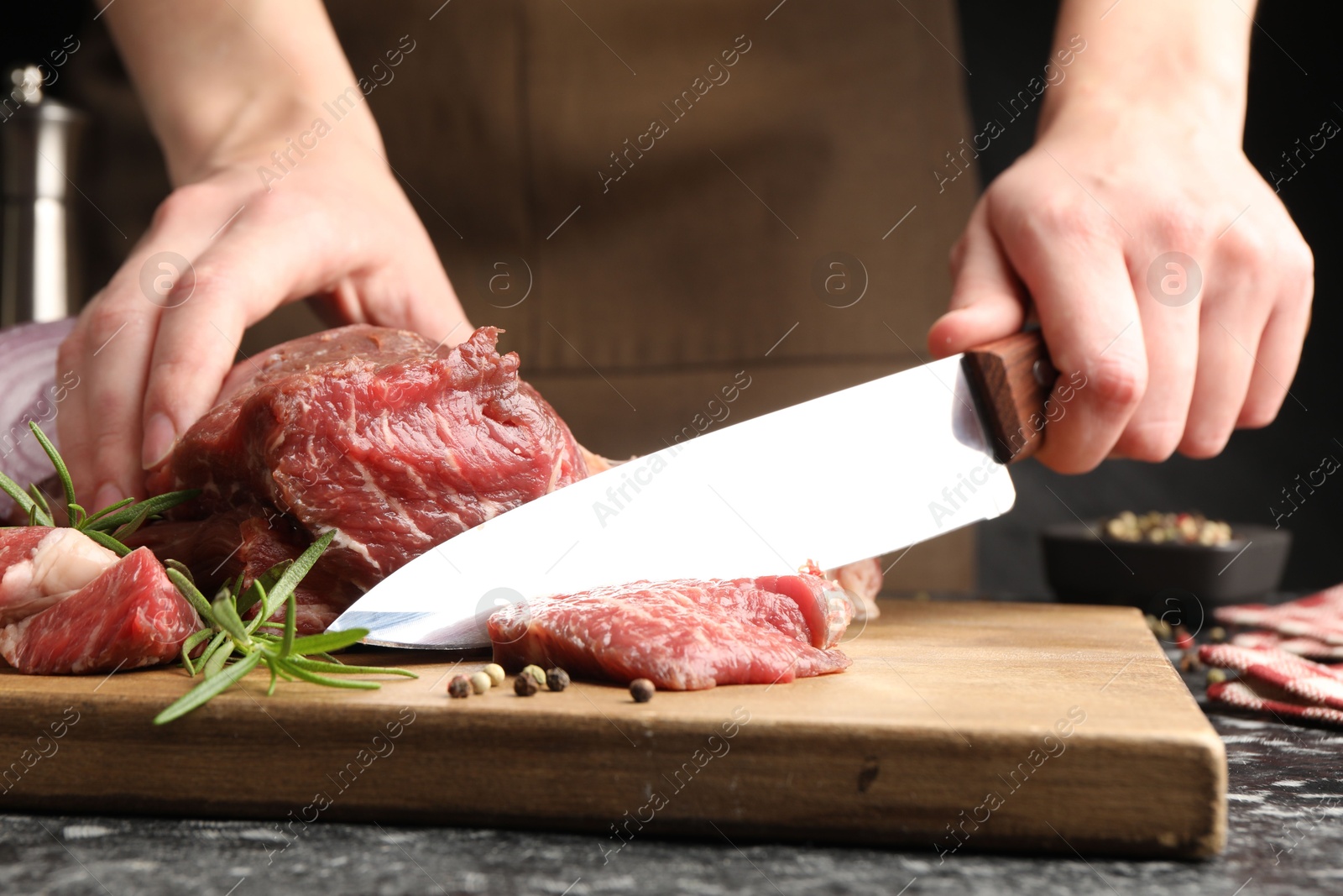 Photo of Woman cutting raw beef meat at dark table, closeup