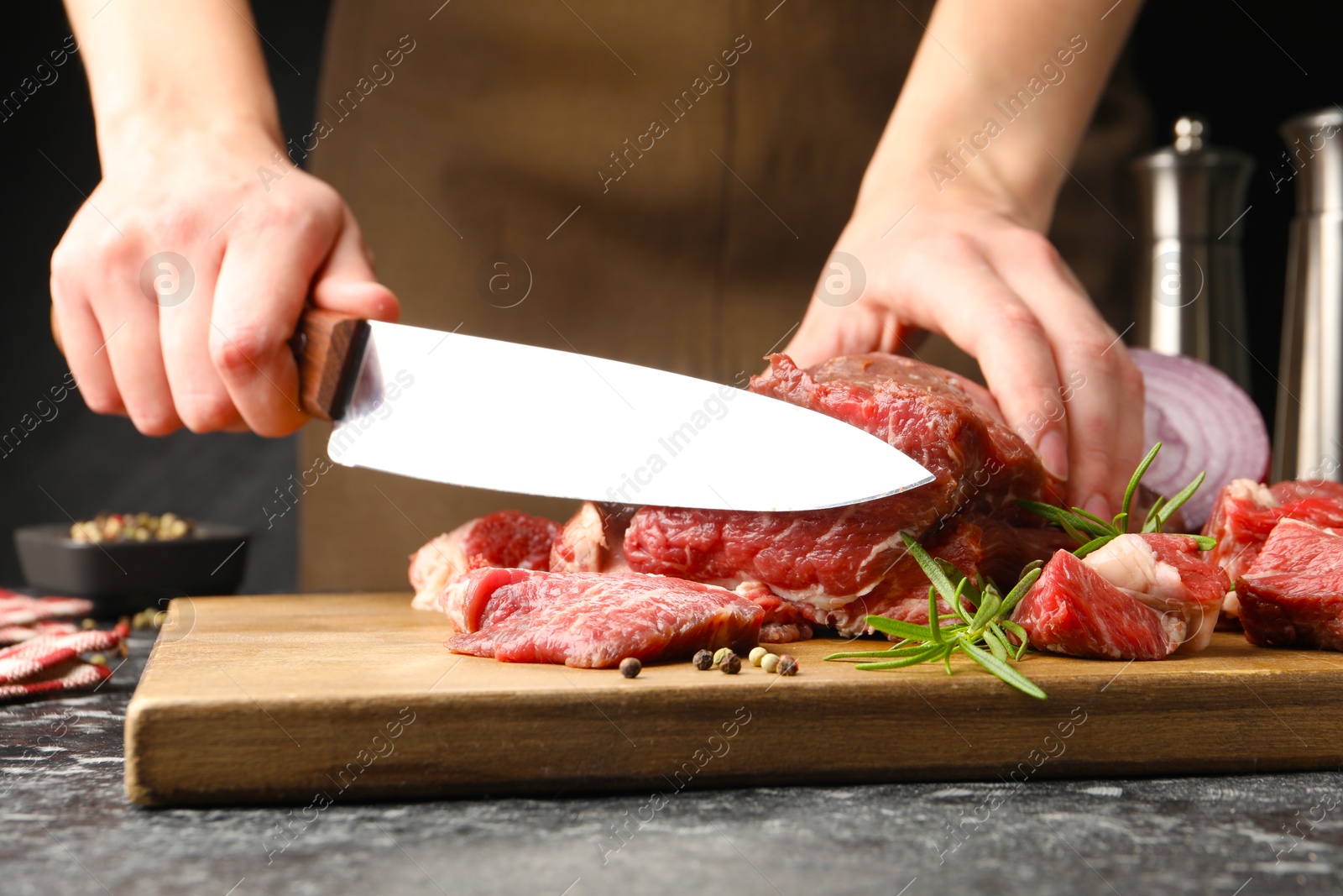 Photo of Woman cutting raw beef meat at dark table, closeup