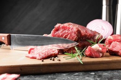 Photo of Pieces of raw beef meat, spices and knife on black marble table, closeup