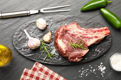 Photo of Piece of raw beef meat, spices and carving fork on black table, flat lay