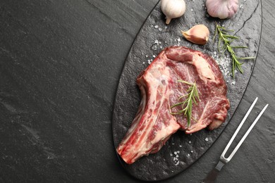 Photo of Piece of raw beef meat, spices and carving fork on black table, flat lay. Space for text