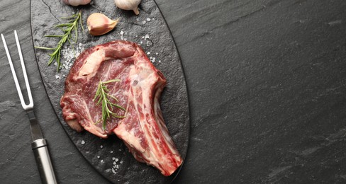 Photo of Piece of raw beef meat, spices and carving fork on black table, flat lay. Space for text