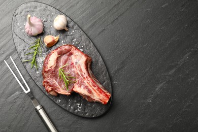 Photo of Piece of raw beef meat, spices and carving fork on black table, flat lay. Space for text