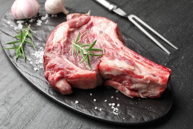 Photo of Piece of raw beef meat, spices and carving fork on black table, closeup