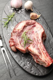 Photo of Piece of raw beef meat, spices and carving fork on black table, above view