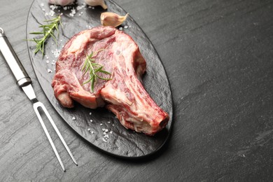 Photo of Piece of raw beef meat, spices and carving fork on black table, above view. Space for text