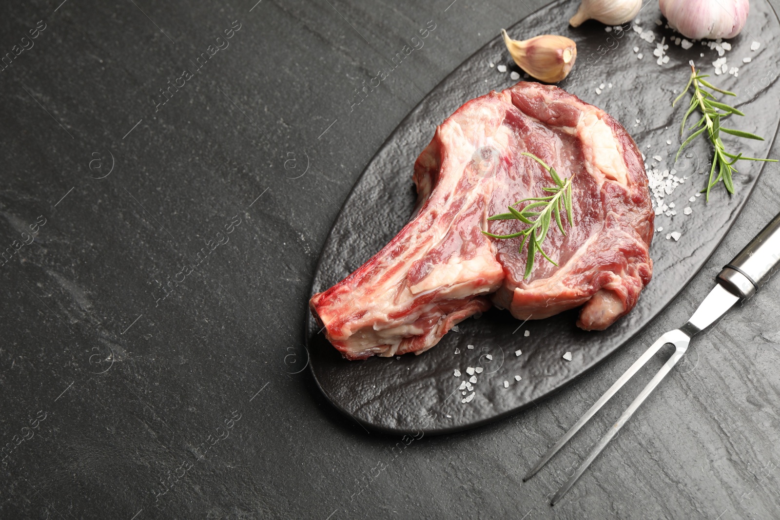 Piece of raw beef meat, spices and carving fork on black table, above view. Space for text Photo of Piece of raw beef meat, spices and carving fork on black table, above view. Space for text