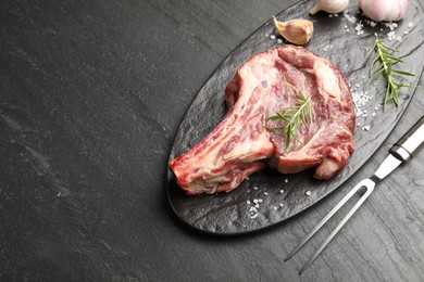 Photo of Piece of raw beef meat, spices and carving fork on black table, above view. Space for text