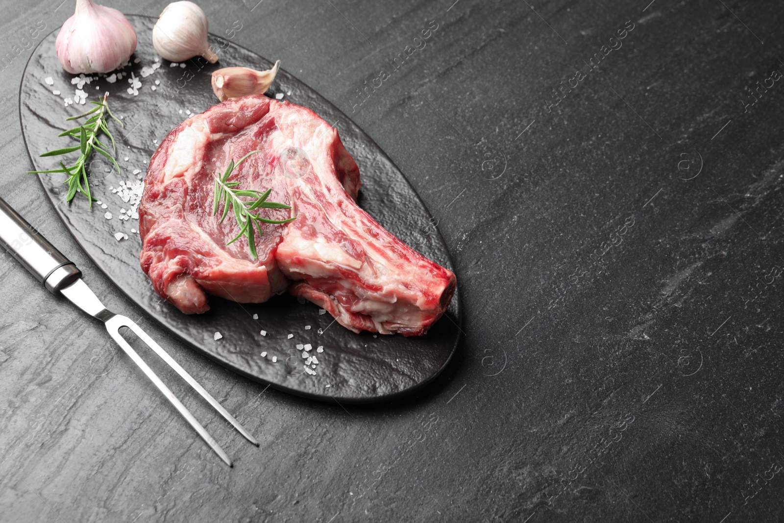 Piece of raw beef meat, spices and carving fork on black table, above view. Space for text Photo of Piece of raw beef meat, spices and carving fork on black table, above view. Space for text