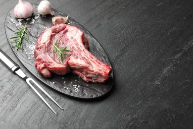 Photo of Piece of raw beef meat, spices and carving fork on black table, above view. Space for text
