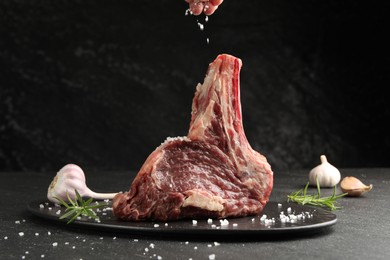 Photo of Woman adding spices to raw beef meat at black table, closeup