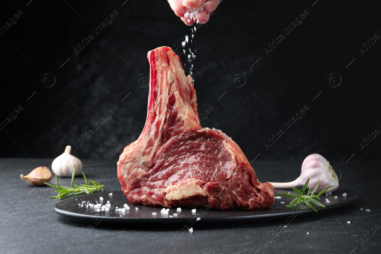 Woman adding spices to raw beef meat at black table, closeup Photo of Woman adding spices to raw beef meat at black table, closeup