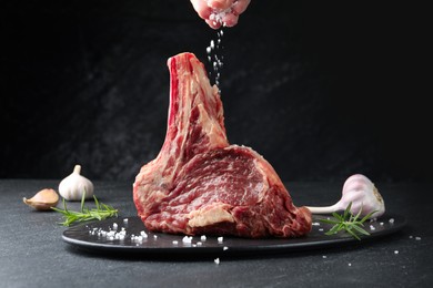 Photo of Woman adding spices to raw beef meat at black table, closeup