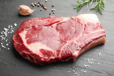 Photo of Piece of raw beef meat and spices on black table, closeup