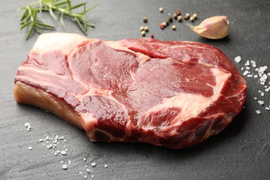 Photo of Piece of raw beef meat and spices on black table, closeup
