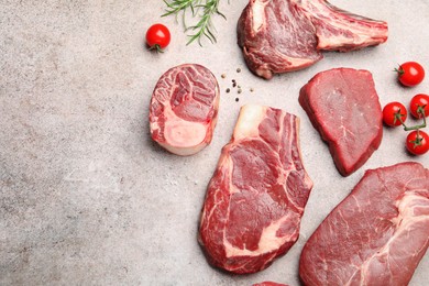 Photo of Pieces of raw beef meat, spices and tomatoes on grey table, flat lay. Space for text