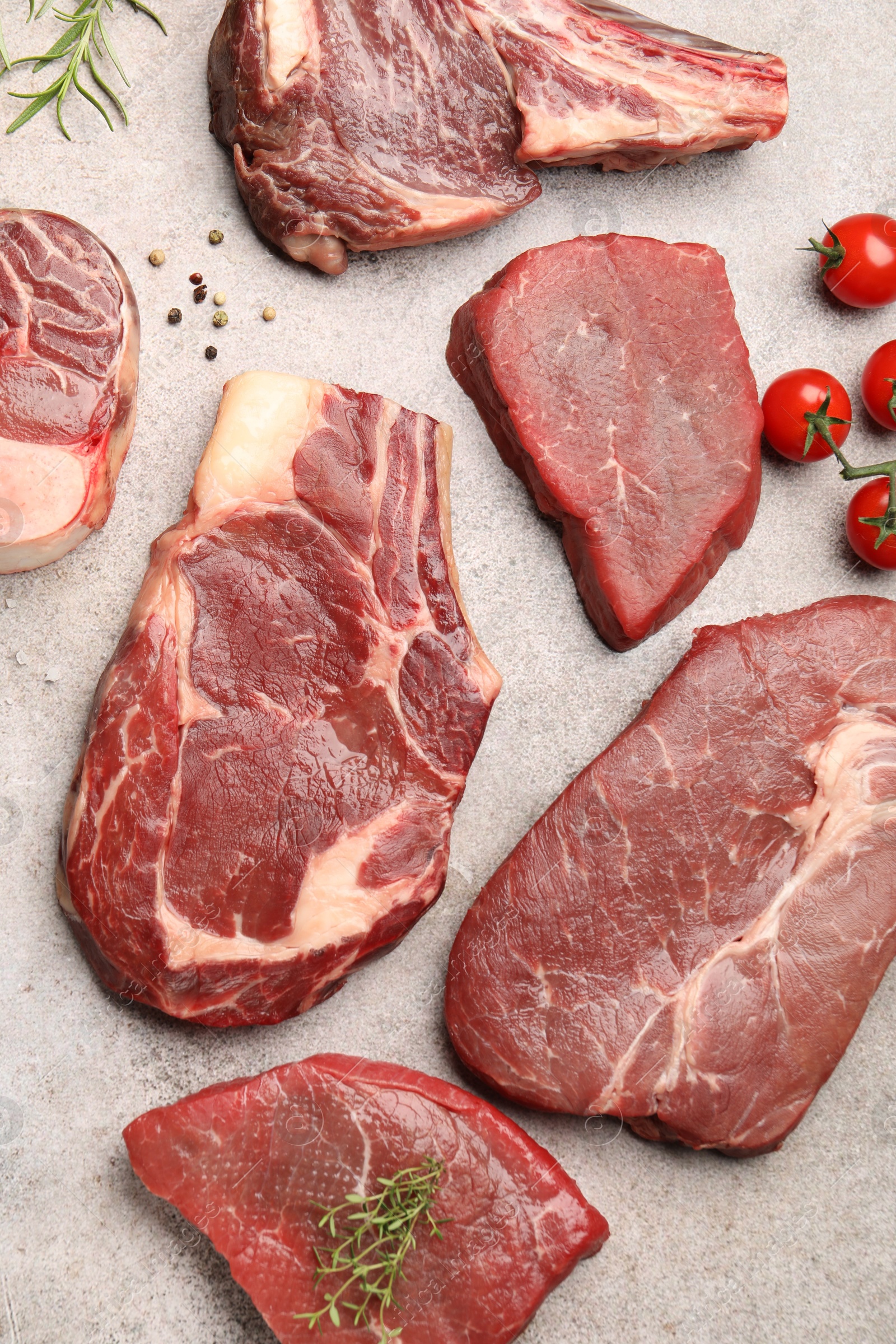 Pieces of raw beef meat, spices and tomatoes on grey table, flat lay Photo of Pieces of raw beef meat, spices and tomatoes on grey table, flat lay