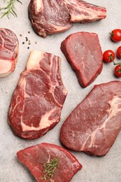 Photo of Pieces of raw beef meat, spices and tomatoes on grey table, flat lay