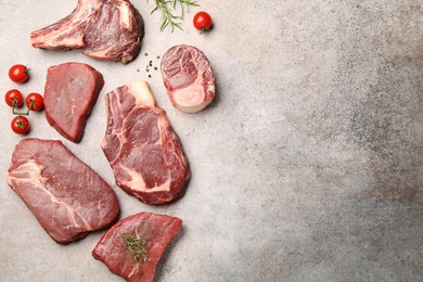 Photo of Pieces of raw beef meat, spices and tomatoes on grey table, flat lay. Space for text