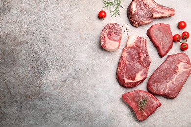 Photo of Pieces of raw beef meat, spices and tomatoes on grey table, flat lay. Space for text
