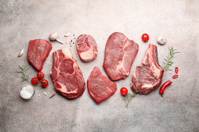 Photo of Pieces of raw beef meat, spices and tomatoes on grey table, flat lay