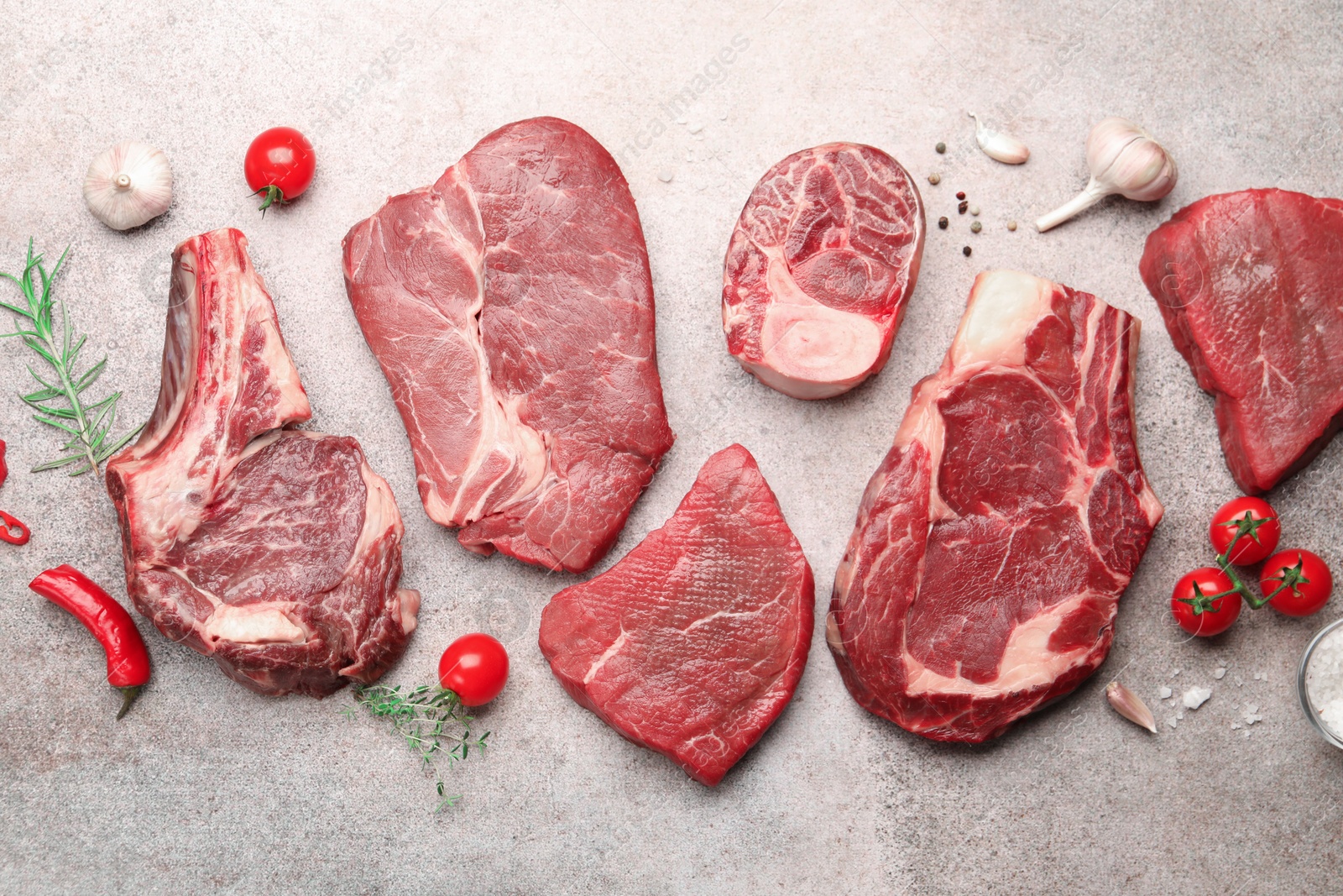 Pieces of raw beef meat, spices and tomatoes on grey table, flat lay Photo of Pieces of raw beef meat, spices and tomatoes on grey table, flat lay