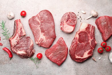 Photo of Pieces of raw beef meat, spices and tomatoes on grey table, flat lay
