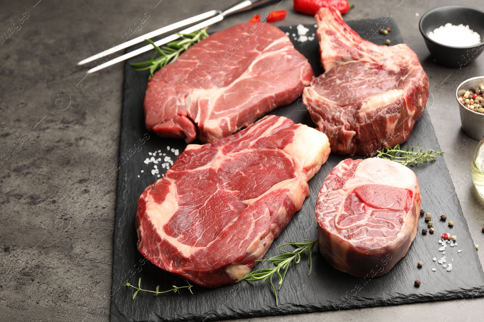 Pieces of raw beef meat, spices and carving fork on grey table, closeup Photo of Pieces of raw beef meat, spices and carving fork on grey table, closeup