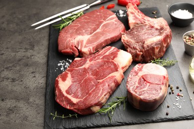 Photo of Pieces of raw beef meat, spices and carving fork on grey table, closeup